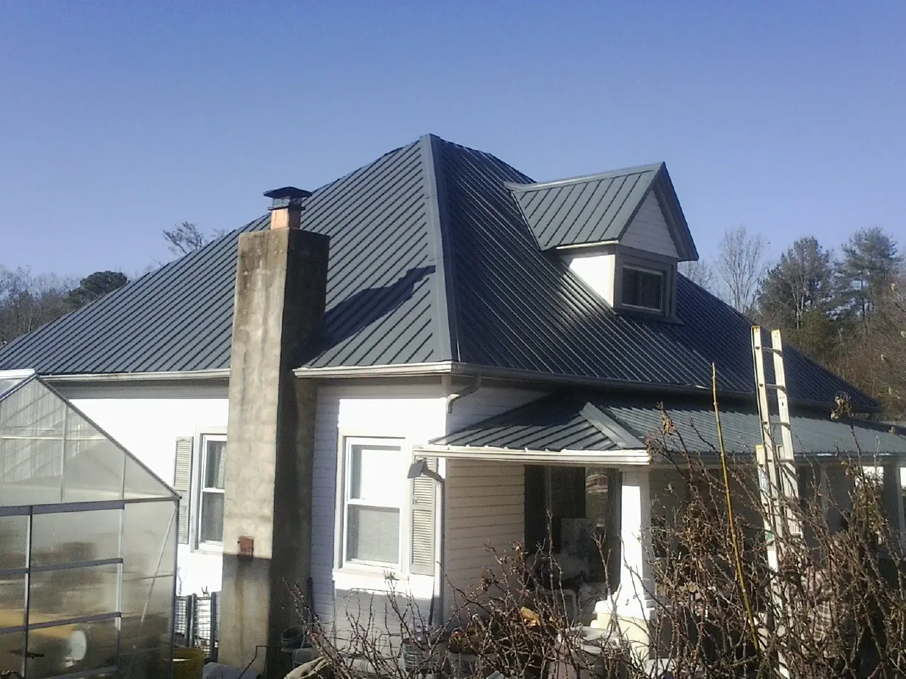 Dark blue standing seam metal roof on a white farmhouse with dormer — Slate & Tile Roof Repair by Roofing Brothers in Debary