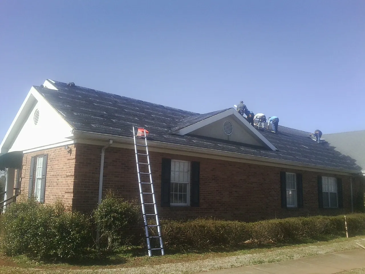 Crew tearing shingles off a brick ranch roof with a ladder set — Emergency Roof Repair work by our crew in Debary