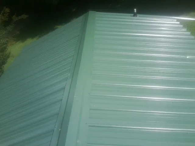 New green metal panels meeting at the ridge of a roof — Flat Roof Repair work by our crew in Debary