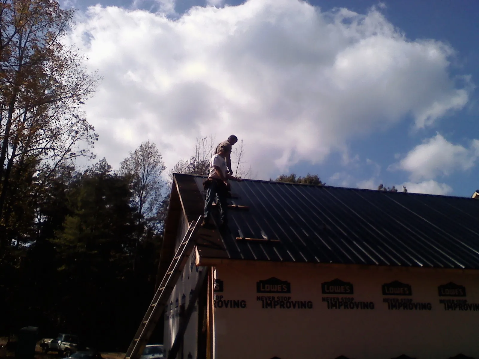 Roofer fastening dark metal panels high against a cloudy sky, from a Roof Inspection job in Debary
