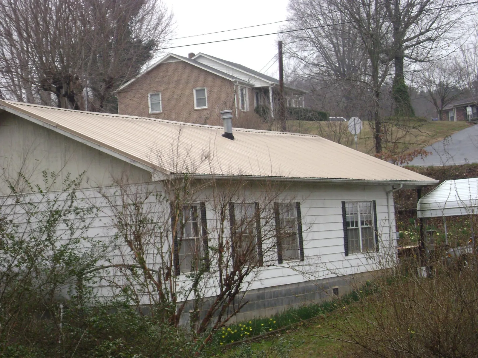 Tan metal roof on a white sided house set into a hillside — Commercial Roofing by Roofing Brothers in Debary